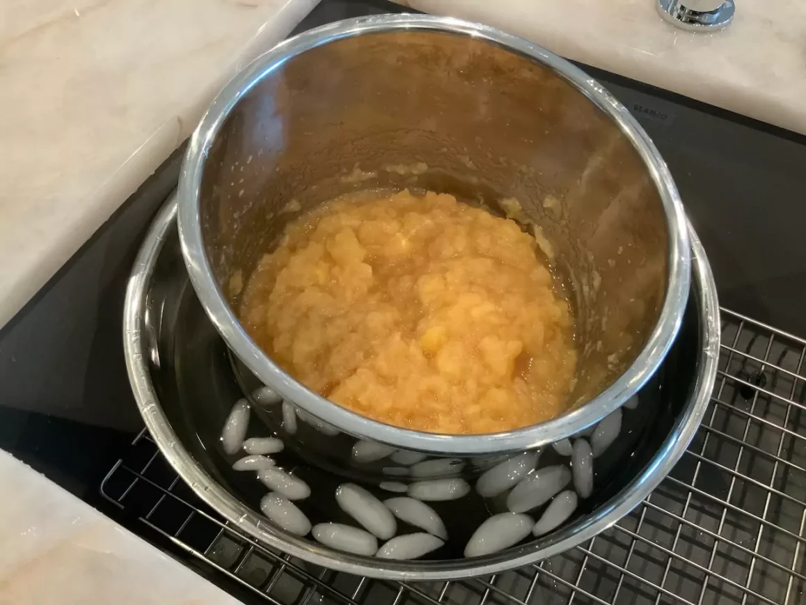 Freshly made Instant Pot applesauce in a metal bowl cooling in an ice bath, resting on a wire rack.